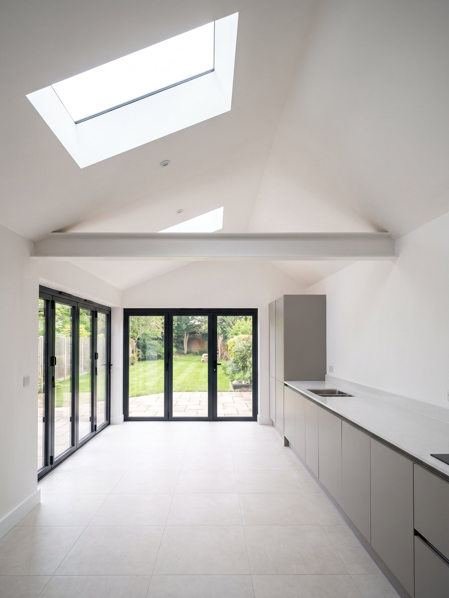 Newly completed rear extension with a vaulted ceiling, roof lanterns and a full wall of black aluminium doors onto the garden