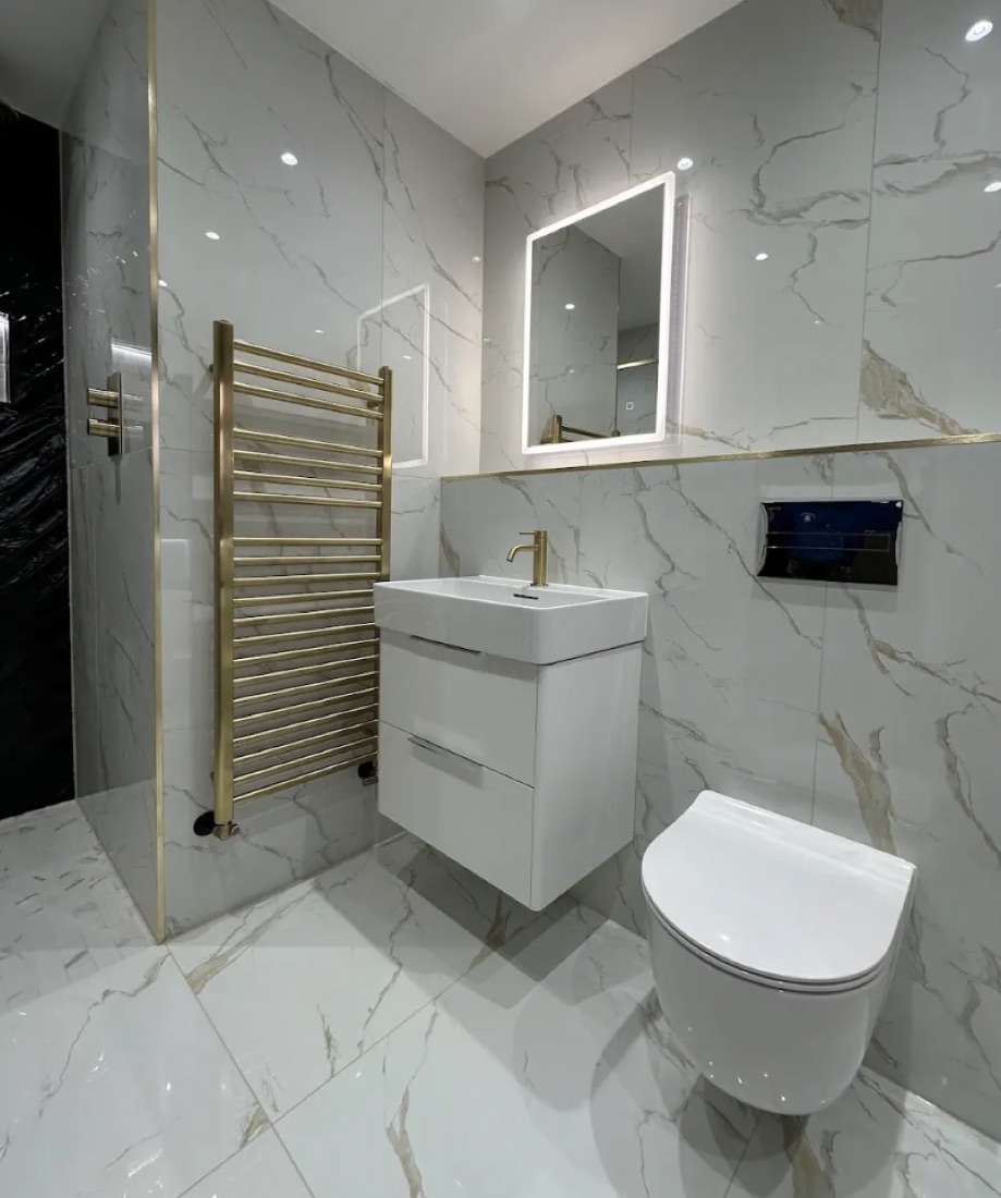 Cloakroom in white-and-gold marble tile with a gold heated towel rail, a wall-hung basin unit and WC