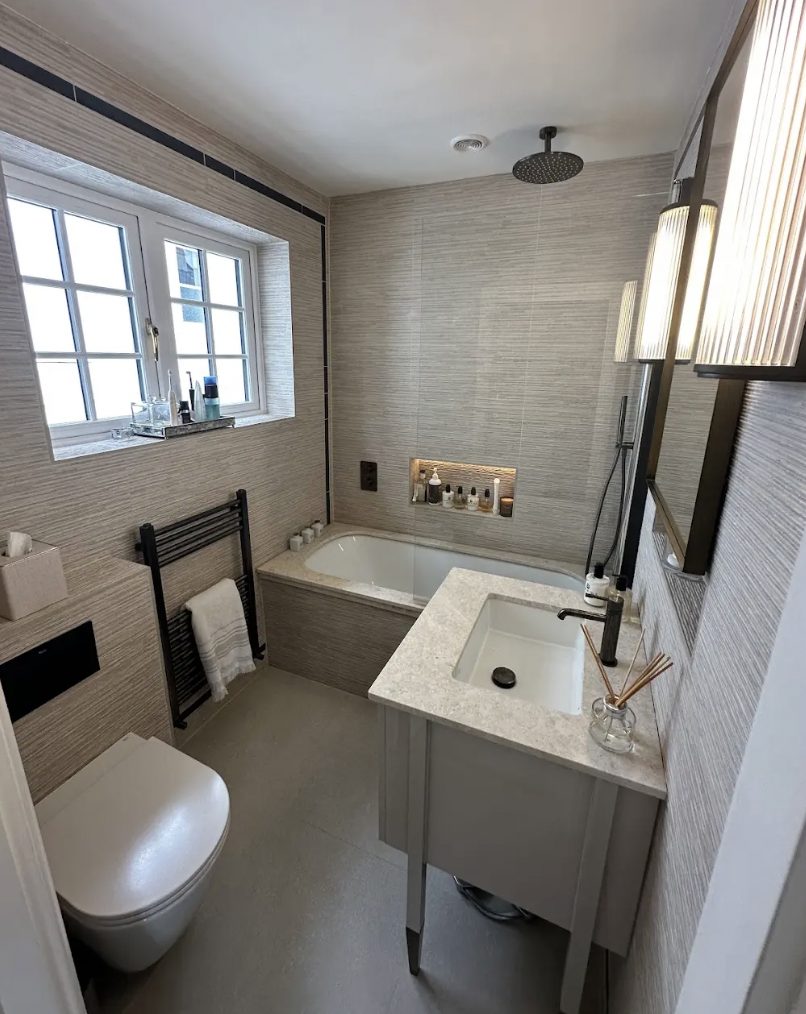 Grasscloth-effect tiled bathroom with a window, bath, fluted vanity and tall sconces