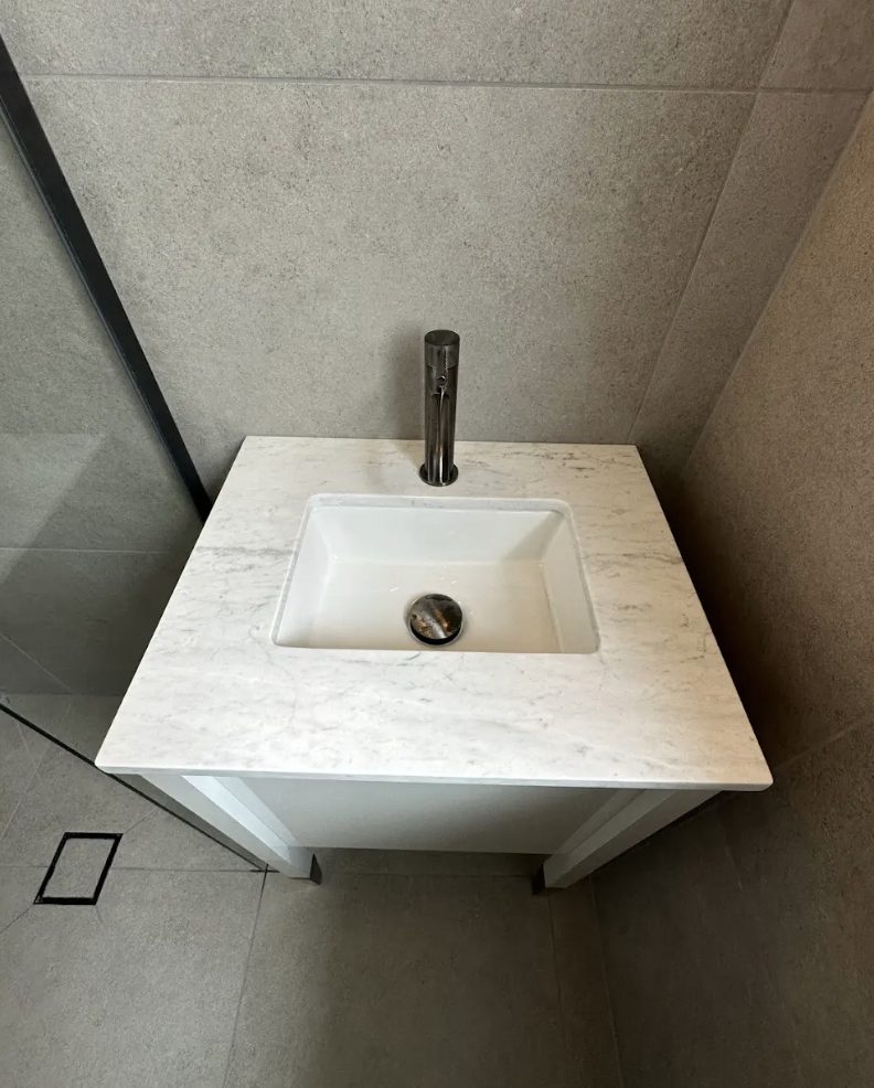 Close detail of an undermount basin set into a marble vanity top with a brushed steel tap