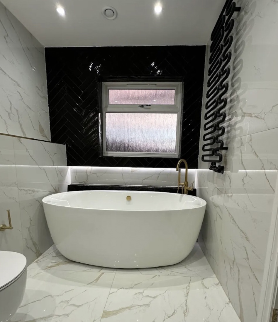Freestanding bath against a black herringbone feature wall with white marble tiling and a gold tap
