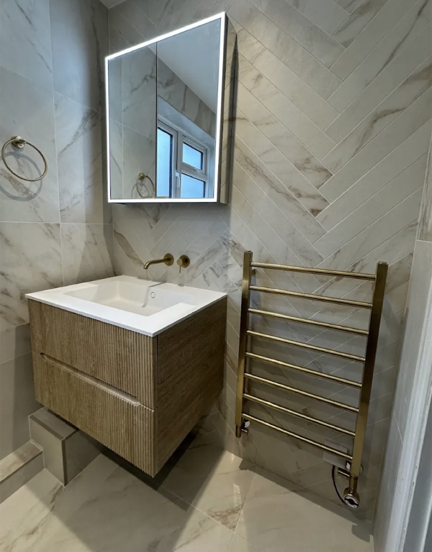 Cloakroom in marble-effect tile with a fluted vanity, a mirrored cabinet and a gold heated towel rail