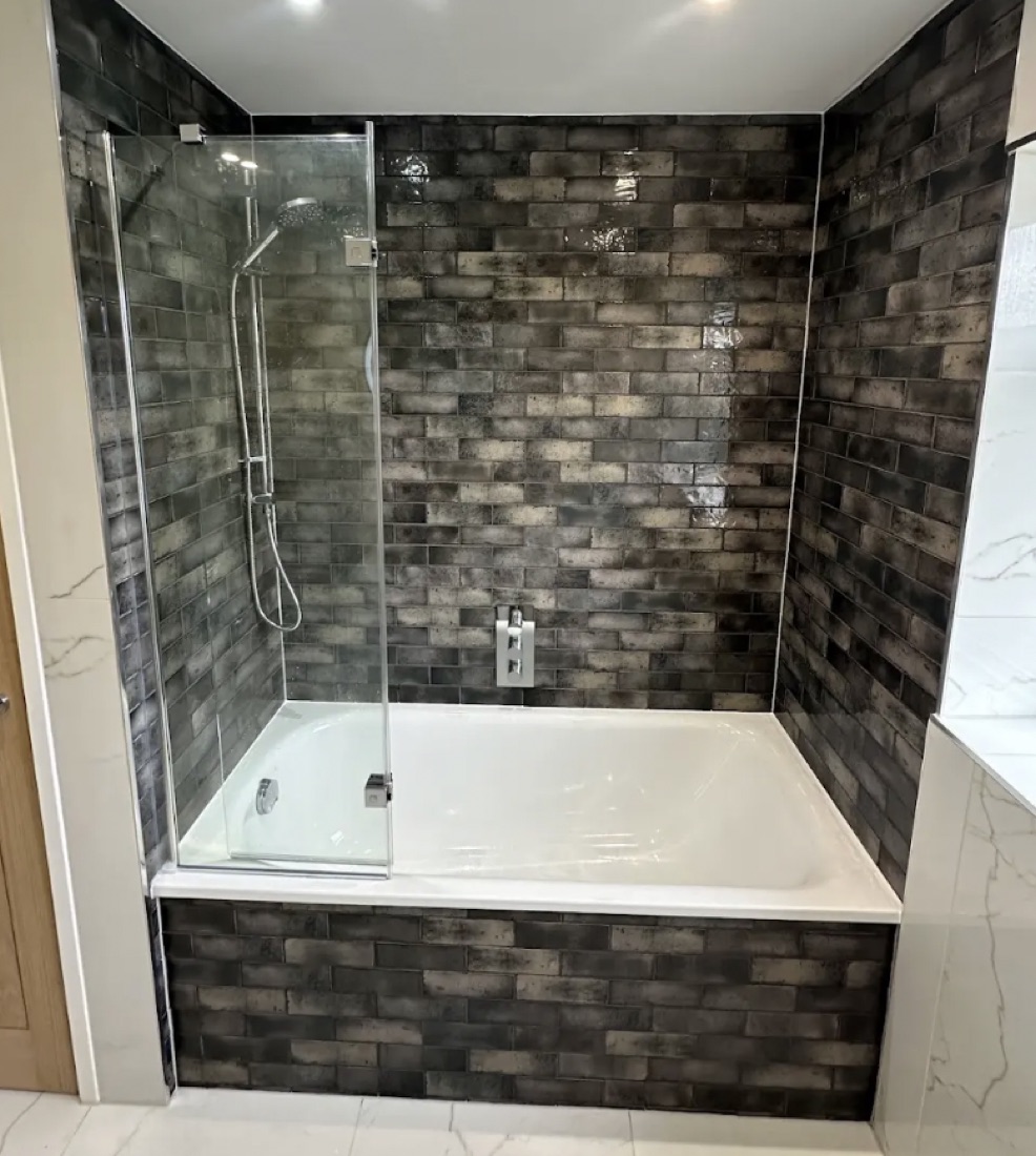 Bath and shower with a dark metallic glazed brick surround and a white marble side wall