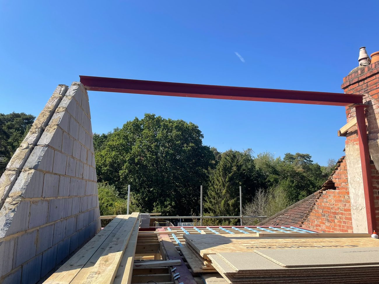 A new red structural steel beam spanning a roof-level opening with the new floor structure going in below