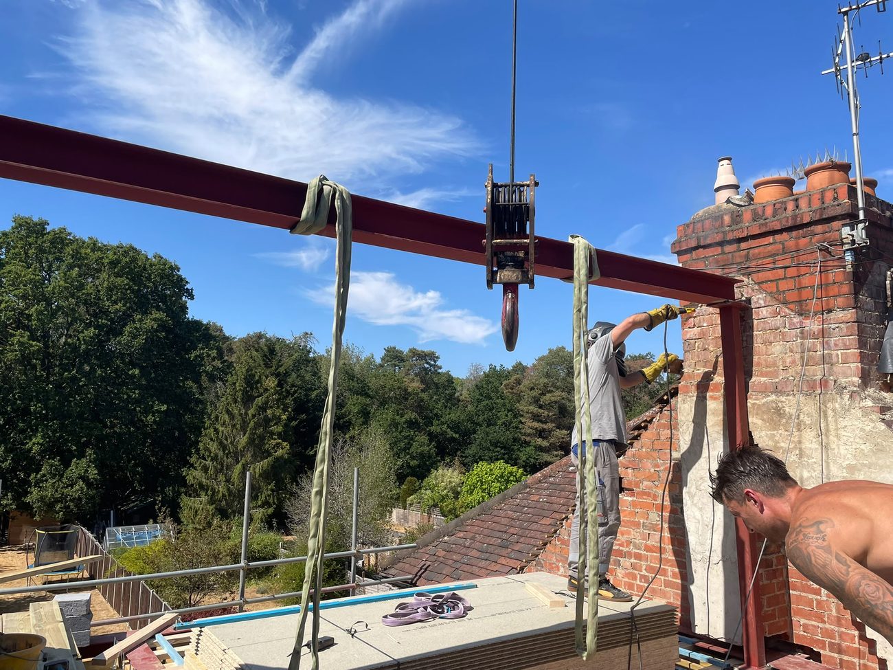 The RS team fixing a craned-in structural steel beam to the brickwork at roof level under a clear blue sky