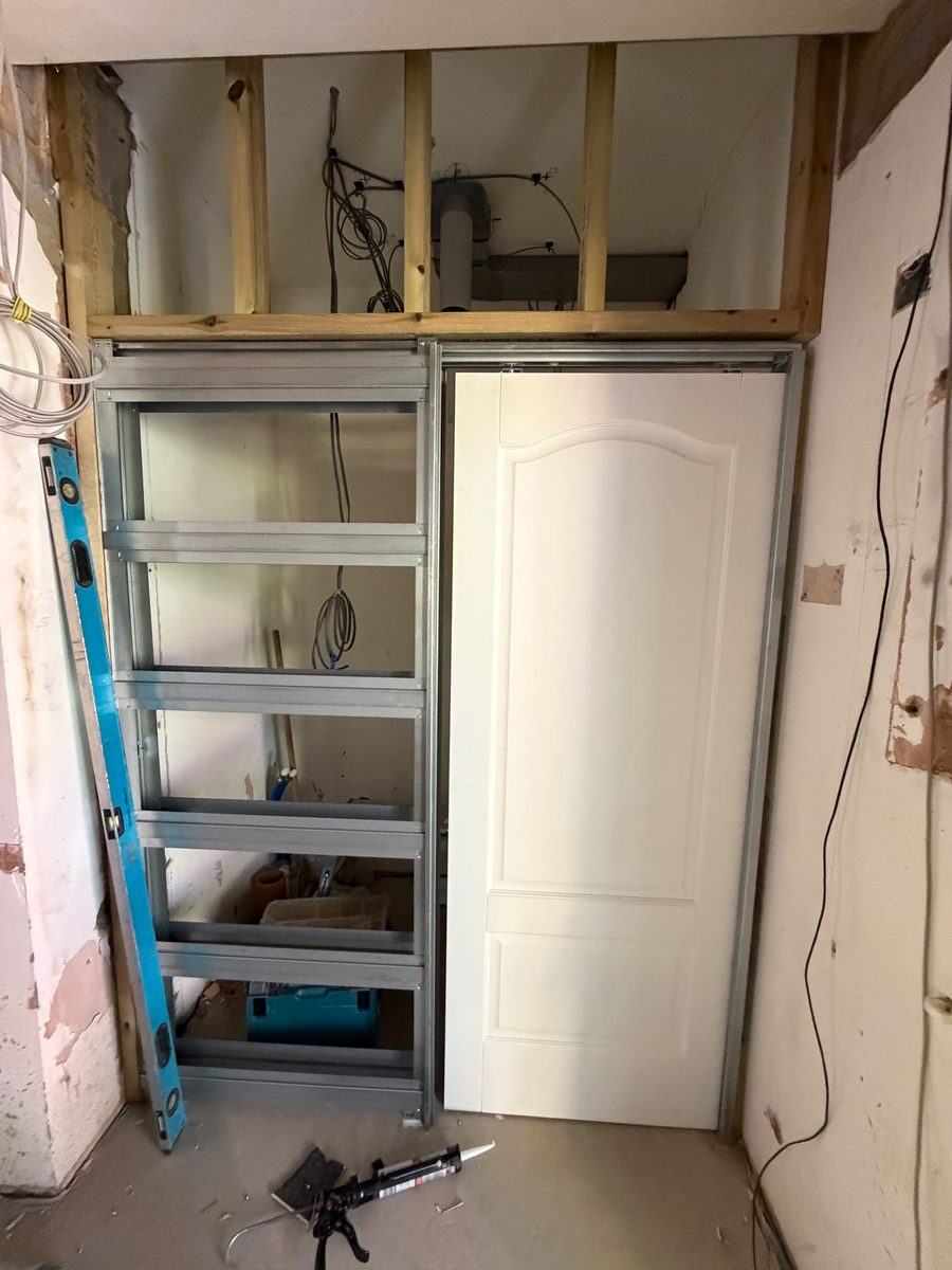 A metal stud partition framed around a doorway during a renovation, with tools and a level